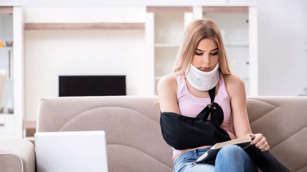 woman sitting on a couch reading book with neck brace and arm in sling